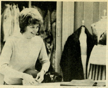 A person on a costume work table looks and smiles in the black and white photo